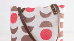 A canvas tote bag with leather handles printed with red circles and brown half moons in Jen Hewitt's Hand-Stamped Tote Bag with Leather Handles class on Creativebug.