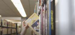 A picture of a hand pulling a book off a library shelf from the Creativebug class Mixtape: Library Love