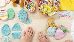 a table top view of hands and Easter crafting items and supplies including re-useable easter eggs, candy and paper