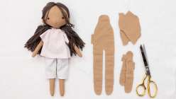 A hand-sewn doll with tan skin wearing a light pink shirt and grey pants made in Katia Ferris's Sew a 14-Inch Rag Doll class on Creativebug.