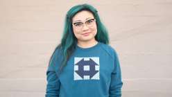 A woman wearing a turquoise sweatshirt with a blue quilt block, made in Faith Hale's Make a Quilt Block Sweatshirt class on Creativebug.