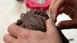A pair of hands stitching yarn hair into a rag doll from Katia Ferris's Creativebug class Rag Doll Hairstyles: Short and Long.
