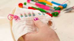 The cuff of a white jumpsuit being embroidered with rainbow-colored threads by Risa Iwisaki Culbertson in her class Wearable Wins on Creativebug